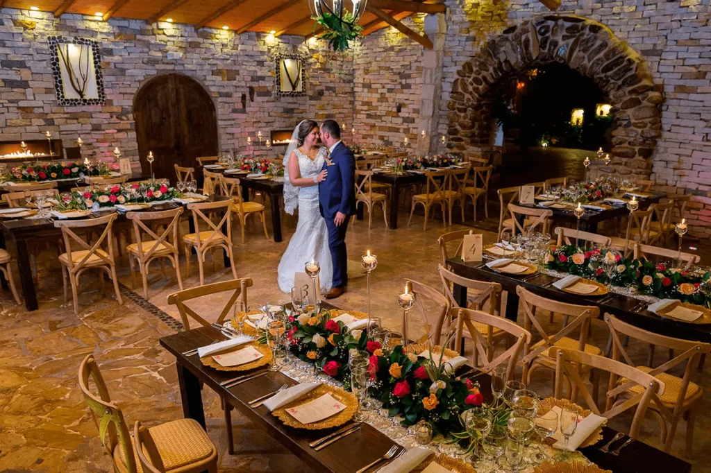 Recepción de matrimonio campestre en un acogedor salón de piedra, con los novios en el centro y mesas decoradas con flores y velas.