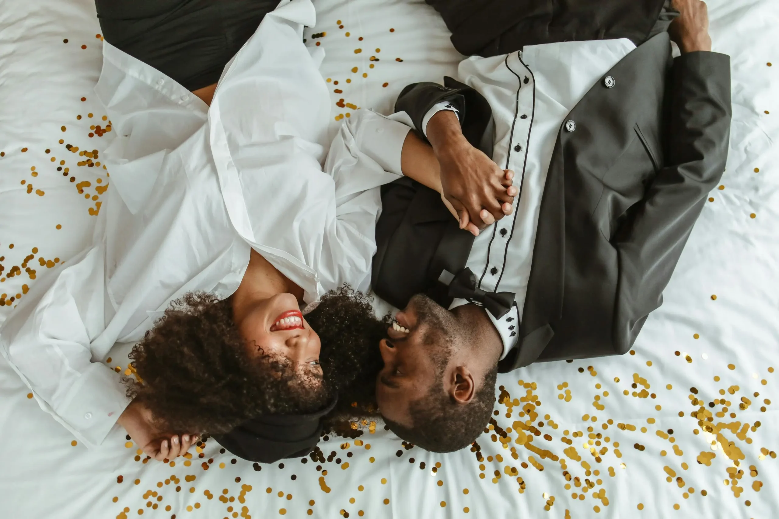 Pareja celebrando su aniversario de bodas de seda acostados entre confeti, reflejando amor y complicidad