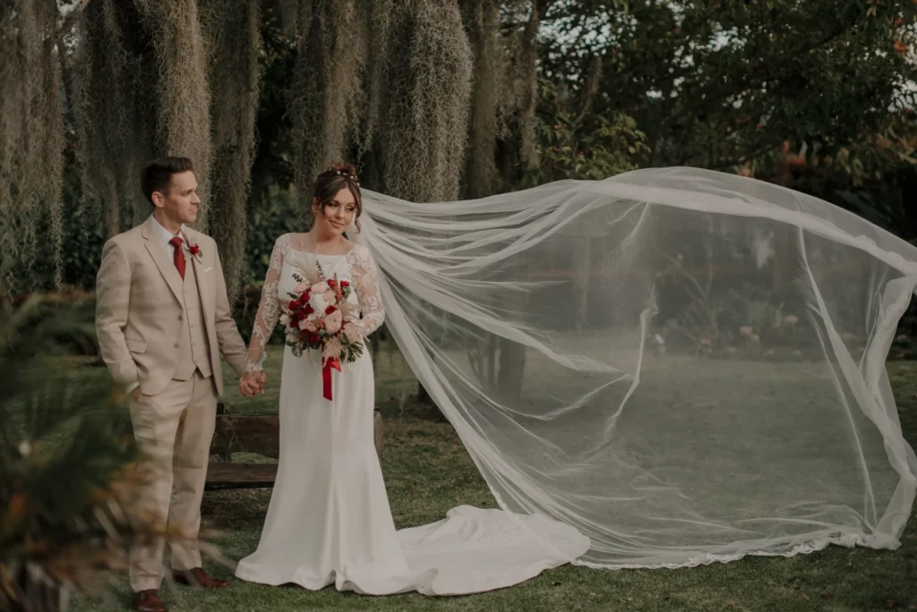 Novios tomados de la mano en exterior con velo al viento, celebrando su matrimonio en Colombia