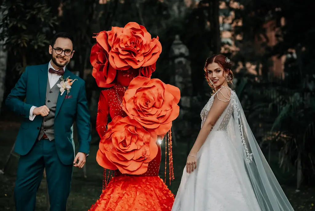 Pareja de novios junto a un performance con vestido de rosas rojas gigantes, ejemplo de personalización en eventos en Bogotá