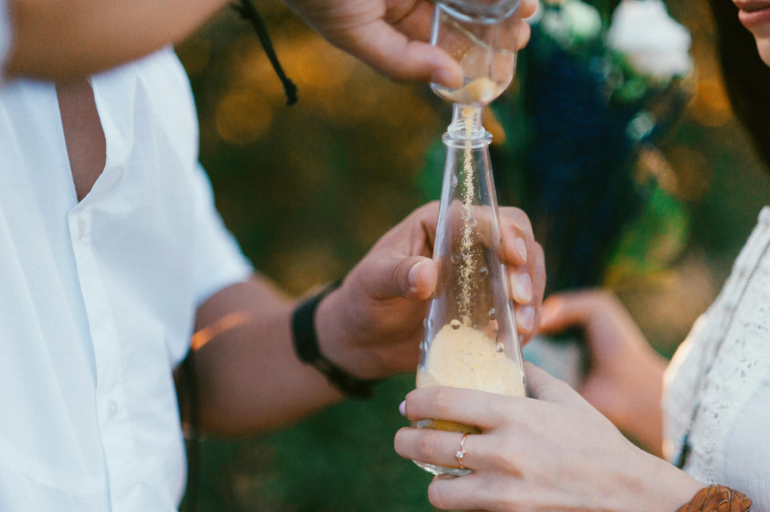 Primer plano de manos realizando la ceremonia de la arena, vertiendo arenas de colores en una botella, simbolizando la unión en una boda espiritual