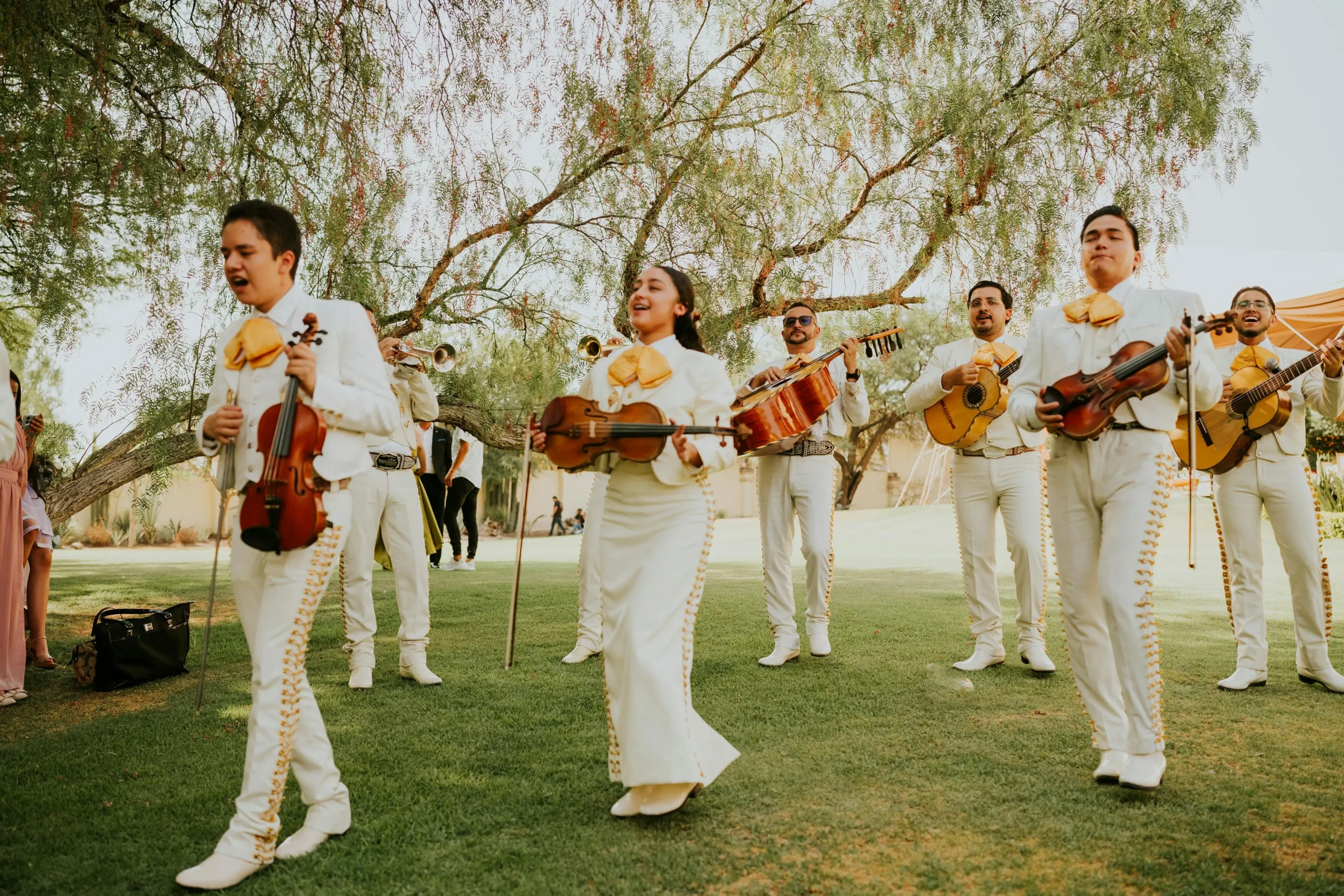 Grupo de mariachis con trajes blancos y amarillos tocando y cantando en un evento campestre en Bogotá, como opción de entretenimiento