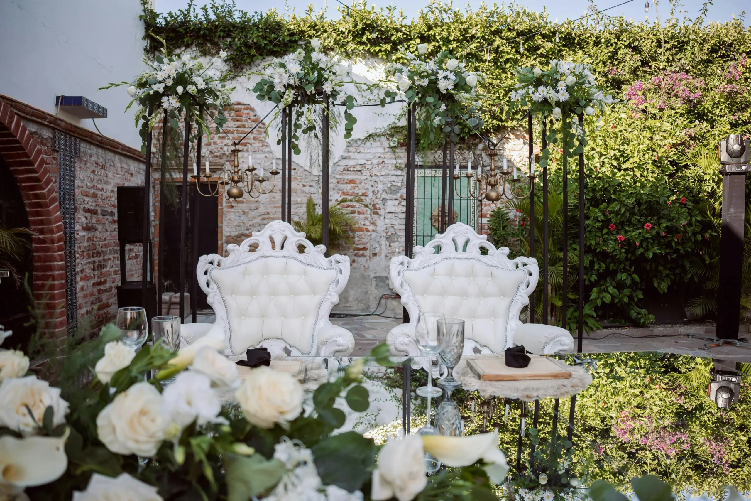 Dos sillas blancas ornamentadas, estilo trono, decoradas con flores blancas y vegetación para una celebración de aniversario al aire libre.