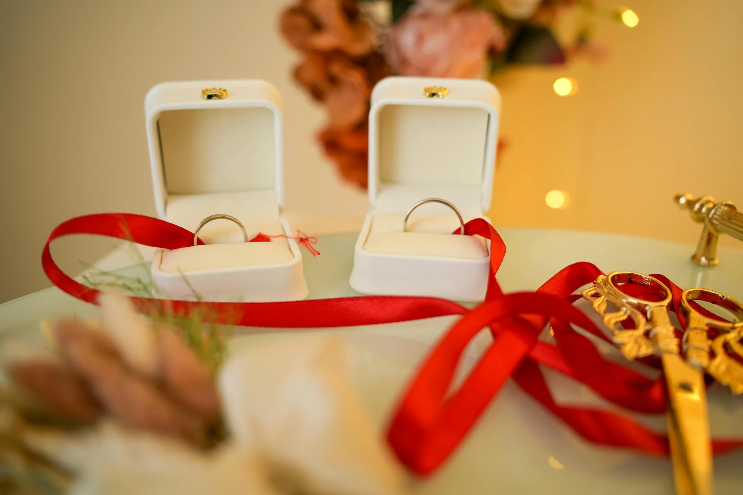 "Anillos de boda en sus cajas abiertas, unidos por un lazo rojo y con tijeras decorativas, detalle de una boda espiritual en Colombia.