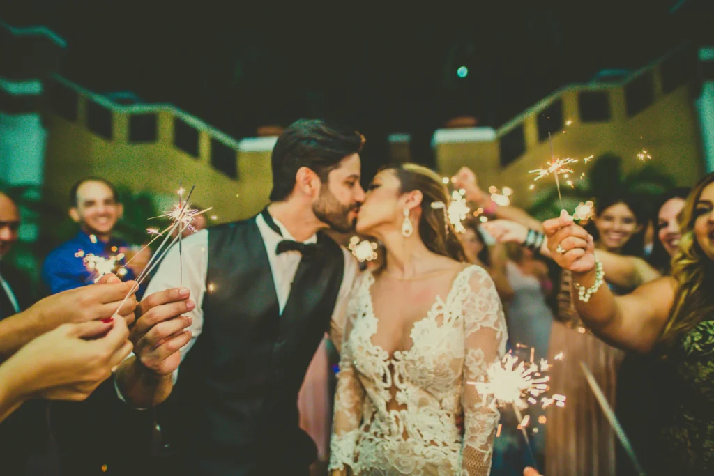 Pareja de novios besándose rodeados de invitados con bengalas encendidas durante la fiesta de su boda en Colombia