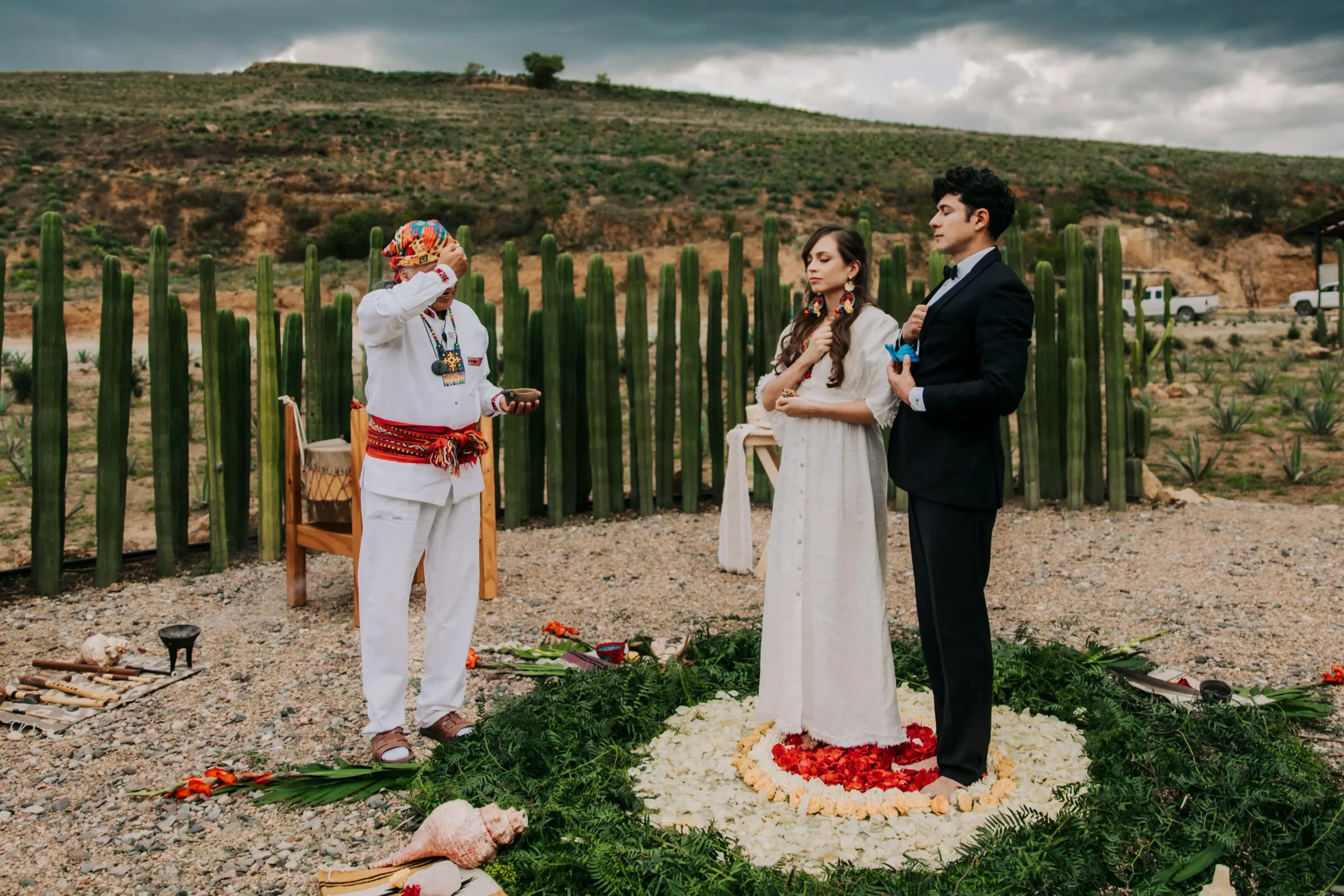 Pareja en una boda espiritual al aire libre en Colombia, de pie dentro de un círculo de pétalos, frente a un oficiante con vestimenta ceremonial