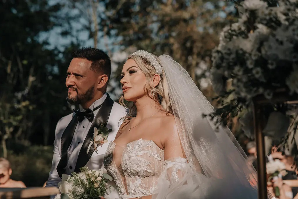  Retrato de novios en un entorno natural; la novia con un elegante vestido de encaje y el novio con esmoquin y corbatín.