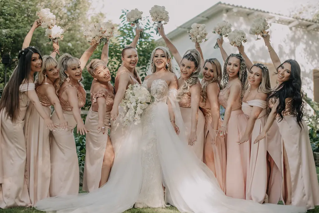 Novia feliz con su ramo de flores blancas, celebrando junto a sus damas de honor vestidas con trajes de color rosa pálido.