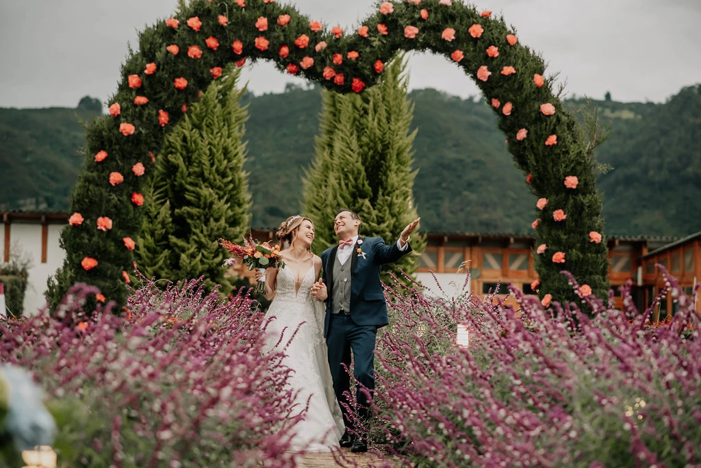 Novios felices celebrando bajo un arco de flores en forma de corazón en su boda campestre en Subachoque.