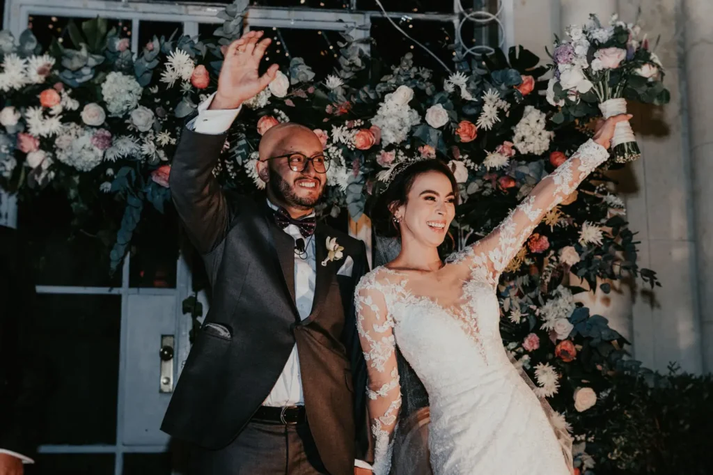 Pareja de novios celebrando con gran alegría en la pista de baile, rodeados de flores, en su casa de eventos en Bogotá.
