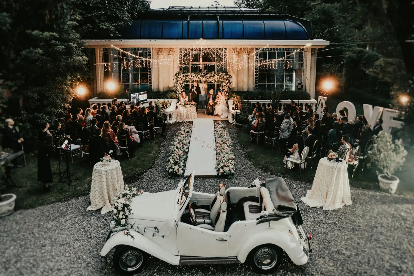 Ceremonia de boda nocturna al aire libre en una exclusiva casa de eventos en Bogotá, con un salón de cristal iluminado de fondo.