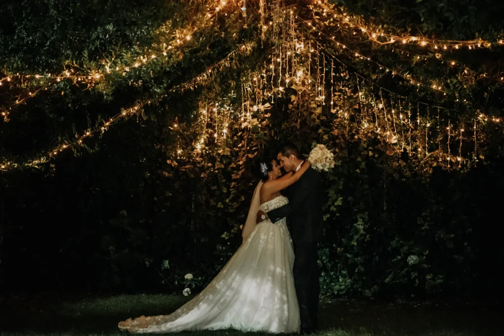 Novios besándose bajo un manto de luces cálidas durante la recepción de su boda en Zipaquirá. La escena nocturna crea un ambiente mágico y romántico
