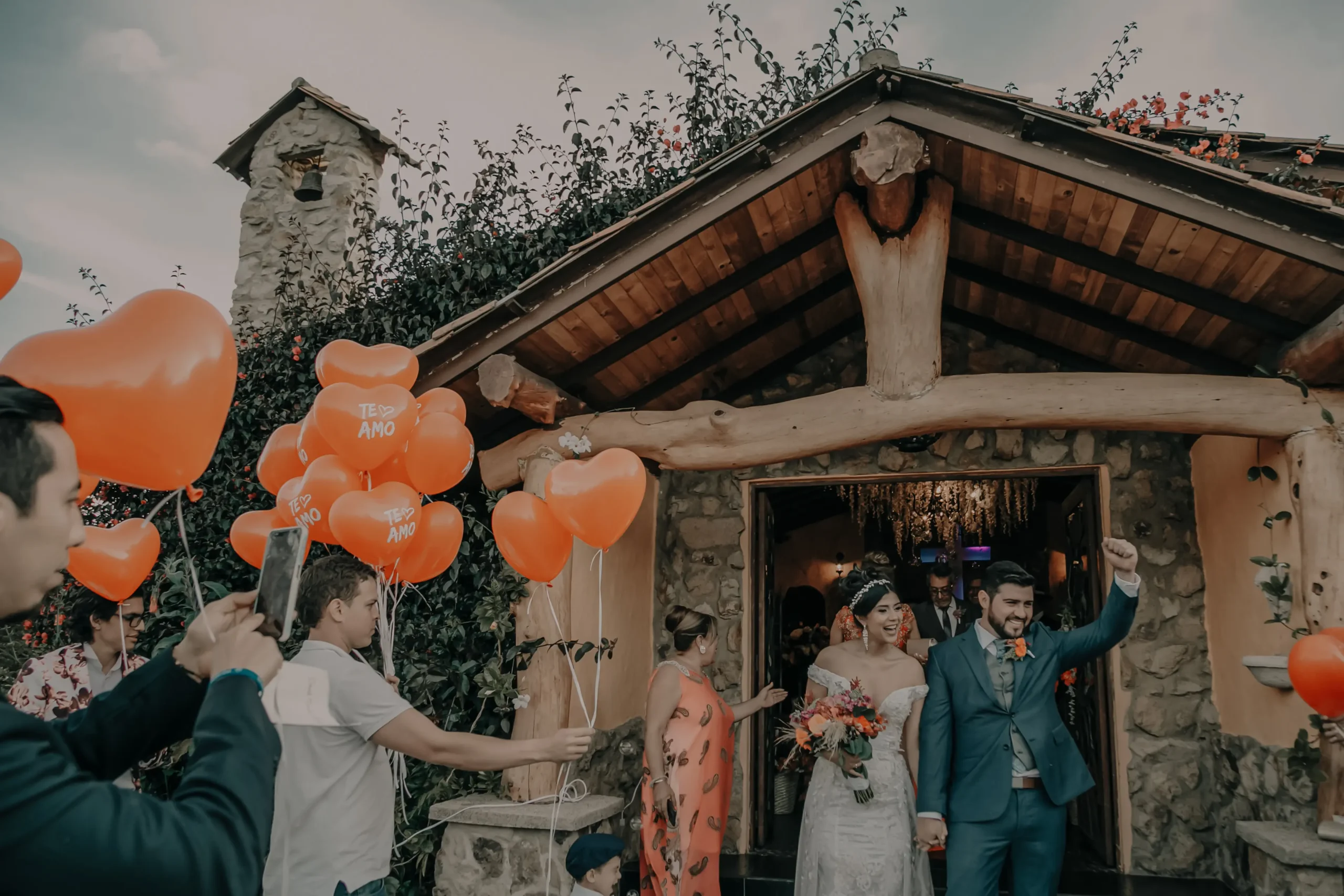 Salida de los novios de la capilla, celebrada por invitados con globos de corazón en una boda en Cajicá.