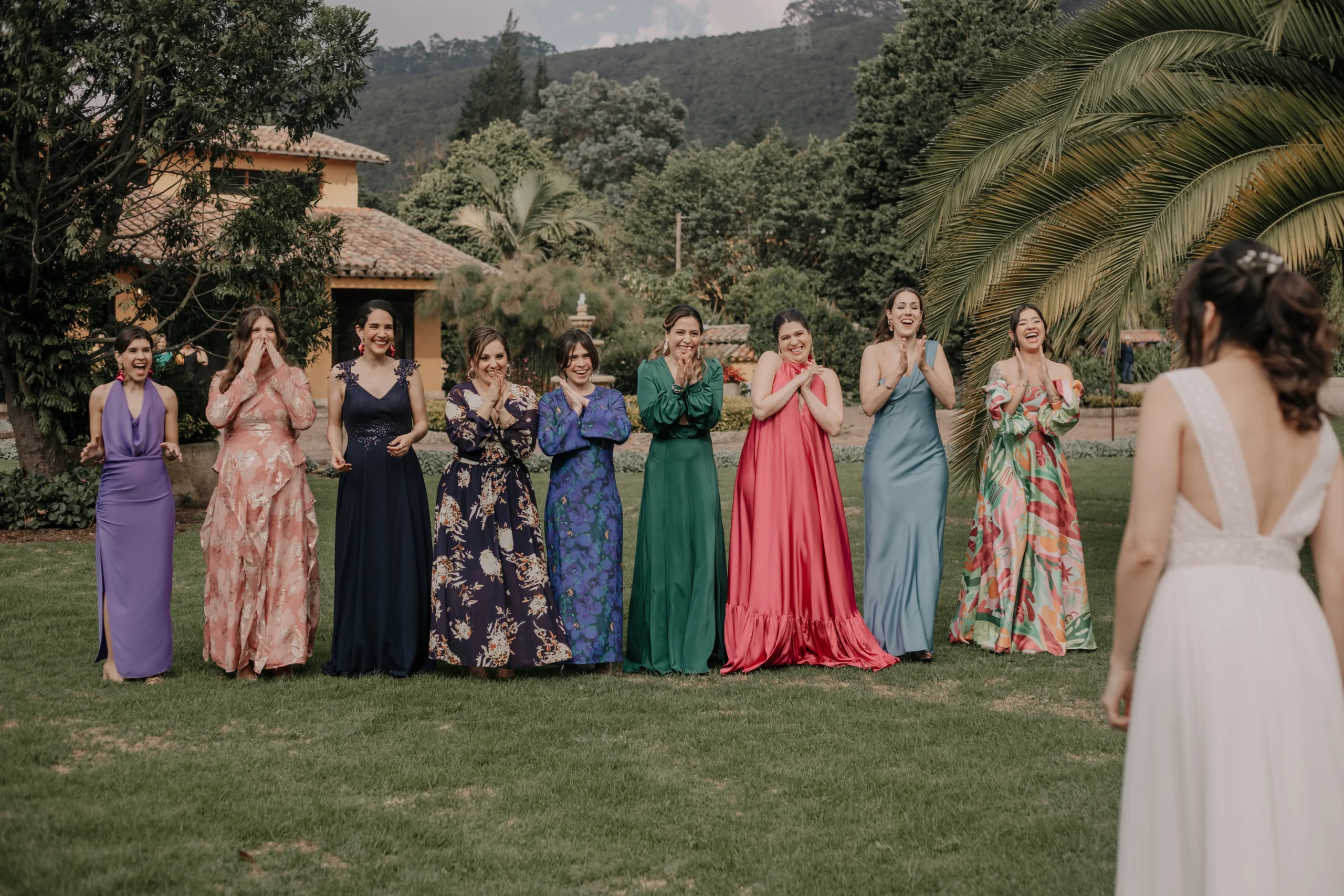 Damas de honor con vestidos largos de diferentes colores aplaudiendo en el jardín de la boda