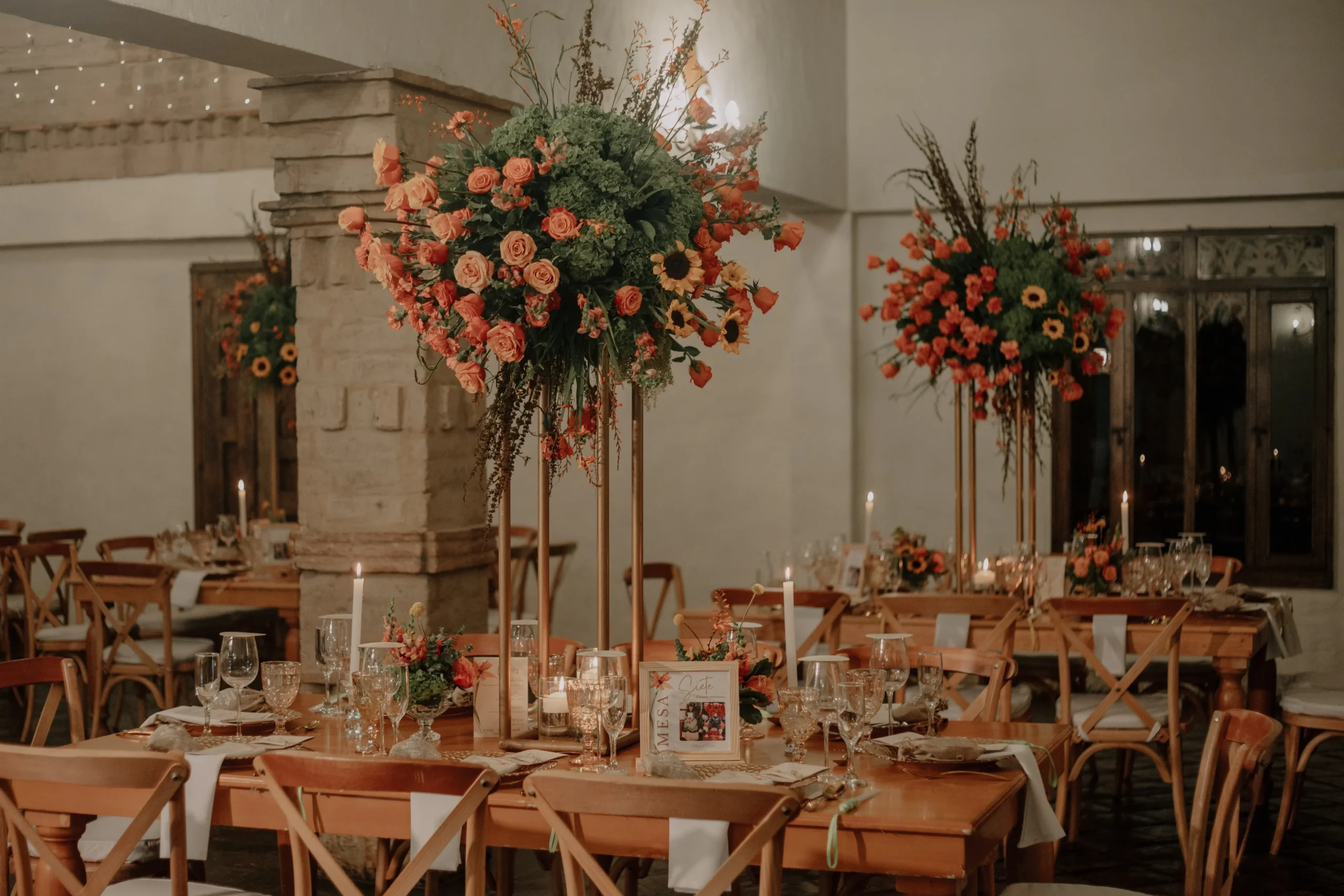 Elegante decoración de mesas para una recepción de boda campestre en Bogotá, con altos centros de mesa florales y velas. 