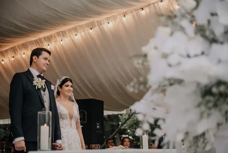 "Pareja de novios al final del pasillo de su ceremonia, bajo una carpa con elegante decoración floral blanca, boda planificada por Eventos Bella Suiza
